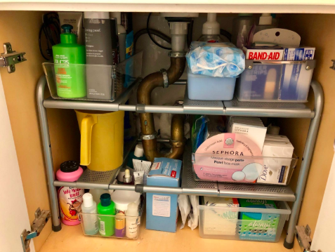 A reviewer's photo showing the inside of a bathroom vanity cabinet, where an adjustable organizer efficiently arranges numerous items in a compact area.