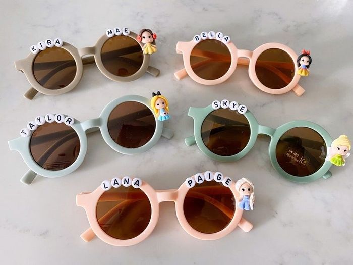 a variety of pastel-colored sunglasses featuring kids' names and Disney characters