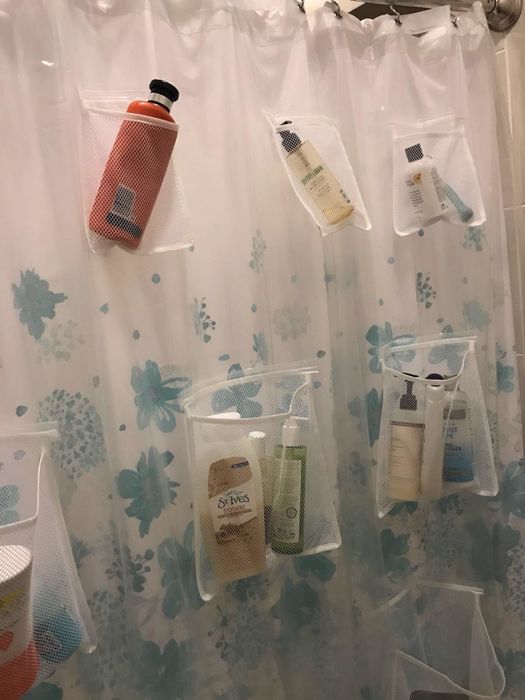 The same clear shower curtain, now holding bottles of shampoo and conditioner in its pockets