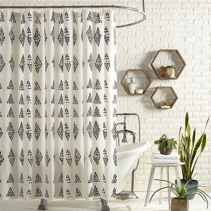A white shower curtain featuring a pattern of black dots arranged irregularly to create a subtle diamond design.