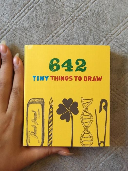a compact book labeled 642 Tiny Things to Draw, held between fingers to emphasize its small size