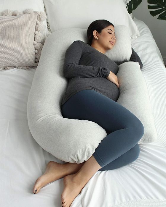 A pregnant model sleeping with the body pillow wrapped around her, leaving space for her arm