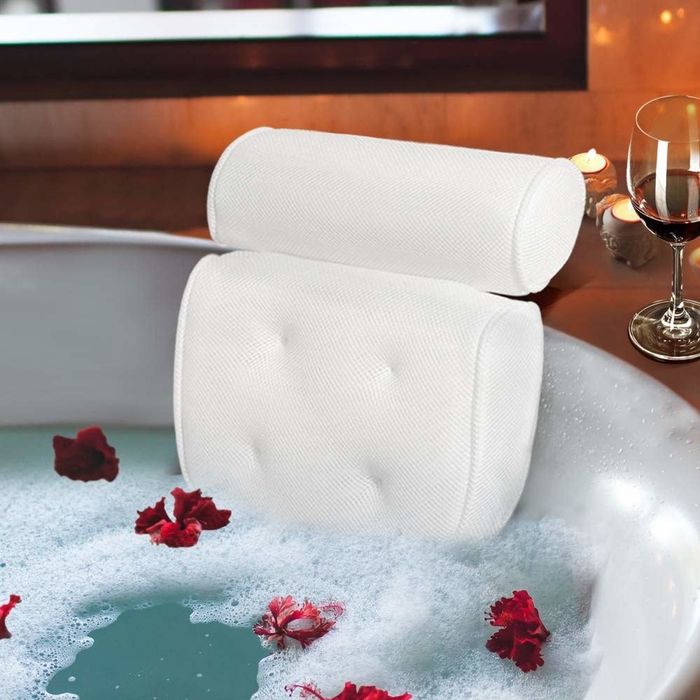 Soft white bath pillow resting on the back of a white tub, surrounded by bubbles and rose petals