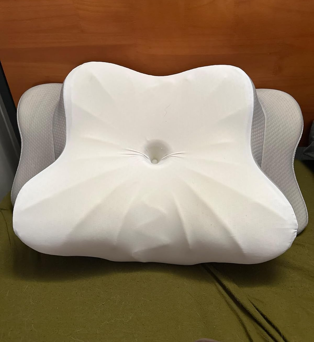 An ergonomic memory foam pillow on a bed, designed to support the neck and spine, with a contoured center for enhanced comfort