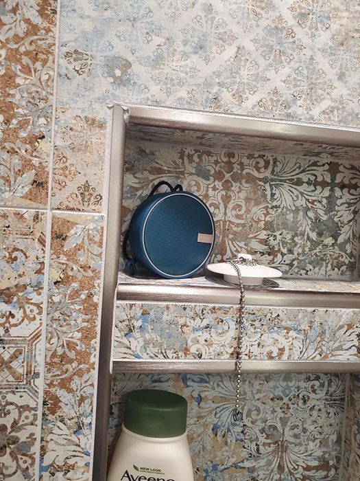 A reviewer's shower shelf features a waterproof speaker neatly placed on top.