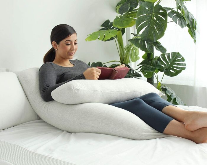 A pregnant model reading a book while resting on the pillow, which supports her book
