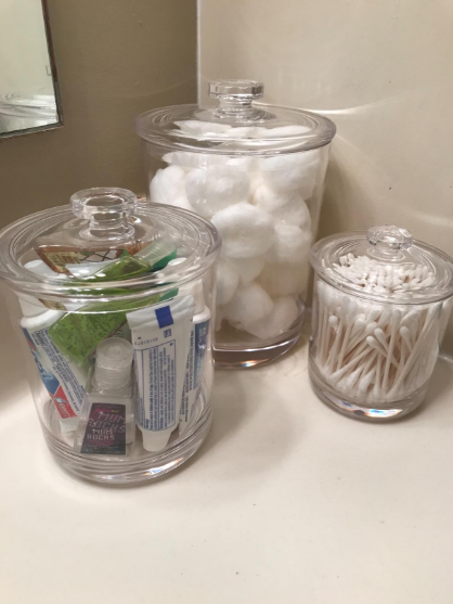 A reviewer-submitted photo showing three transparent plastic jars filled with assorted toiletries, neatly arranged on a bathroom sink.