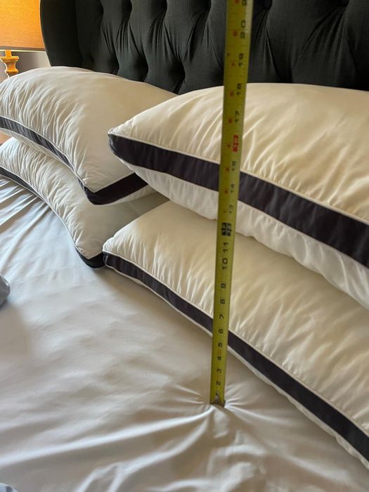 A measuring tape displaying the thickness of luxurious pillows on a bed