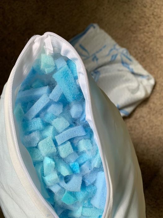 A pillow with its zipper partially open, exposing the shredded memory foam filling inside. A pillowcase is visible on the floor nearby