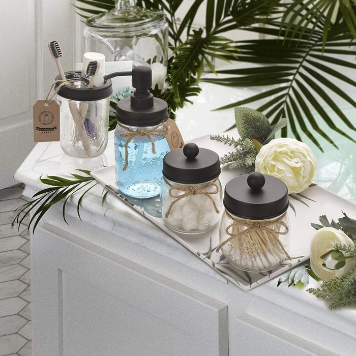 Mason jars filled with mouthwash, toothbrushes, and cotton swabs sitting on a white bathroom counter