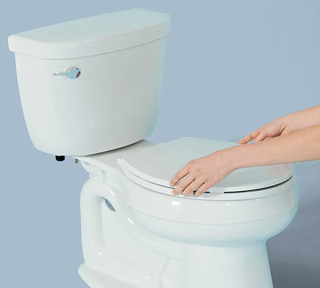 Hands installing the white Tushy bidet attachment on a white toilet