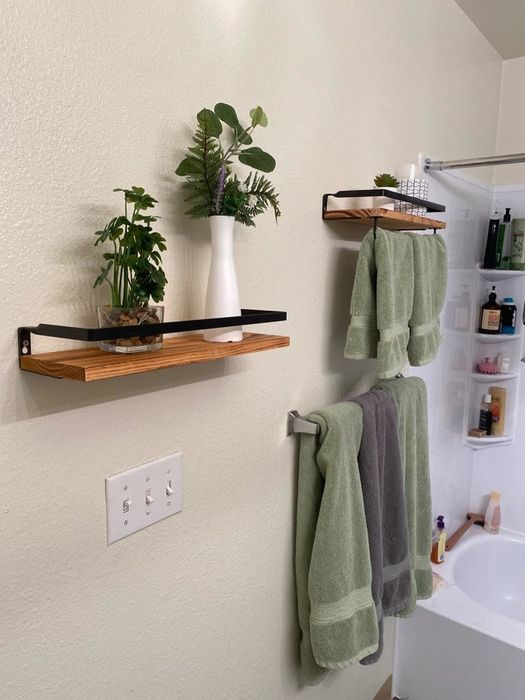 Brown floating shelves adorned with white plant vases and green towels hanging below