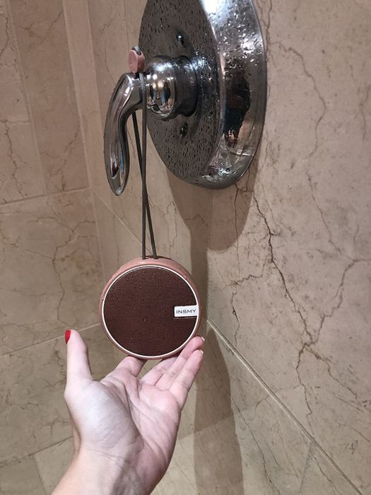 A reviewer is pictured holding a shower speaker attached to the shower handle.
