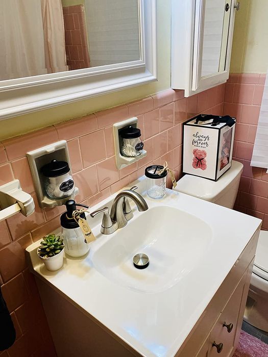 The same mason jar set resting on a bathroom sink beneath pink-tiled walls