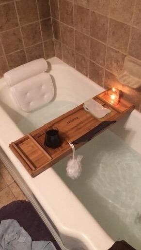 The same pillow on a white tub, paired with a bath caddy and running water