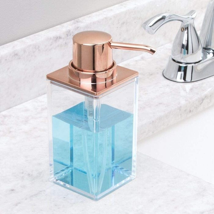 A sleek soap dispenser with rose gold detailing placed on a bathroom sink
