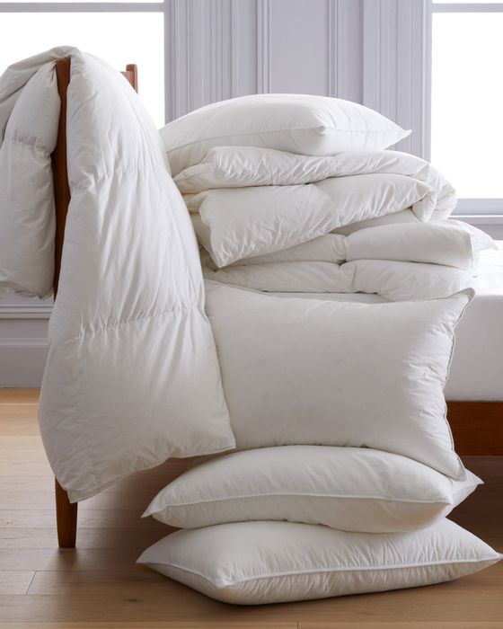 A collection of plain white pillows and comforters in various sizes, arranged in a minimalist room setting, evoking a sense of cozy bedding options