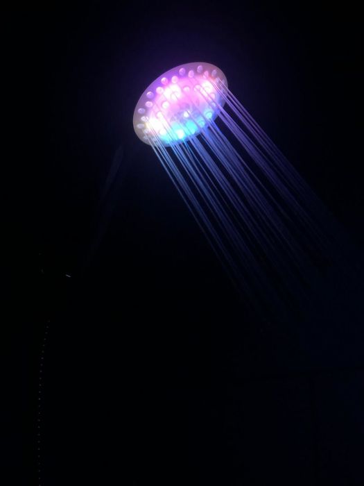 An LED showerhead casting purple light in a completely dark bathroom