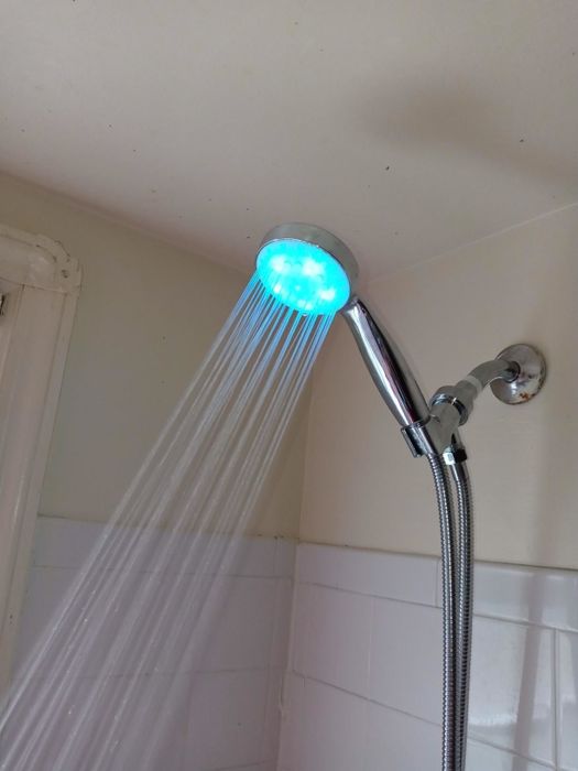 Blue light shining from an LED showerhead in a white-tiled shower