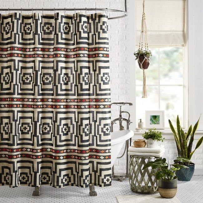 A red, navy blue, orange, and white-patterned shower curtain hanging in front of a vintage claw-foot bathtub