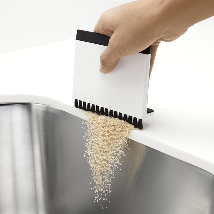 A hand using the brush side to sweep crumbs directly into the sink