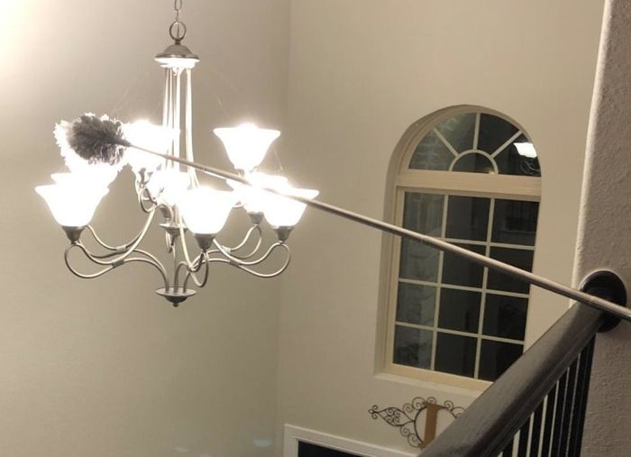 Amazon reviewer using the duster to clean a lamp hanging in the middle of a hallway