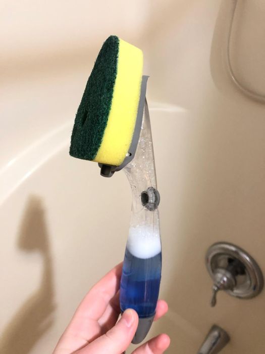 A reviewer holding a dish scrubber with a built-in soap dispenser