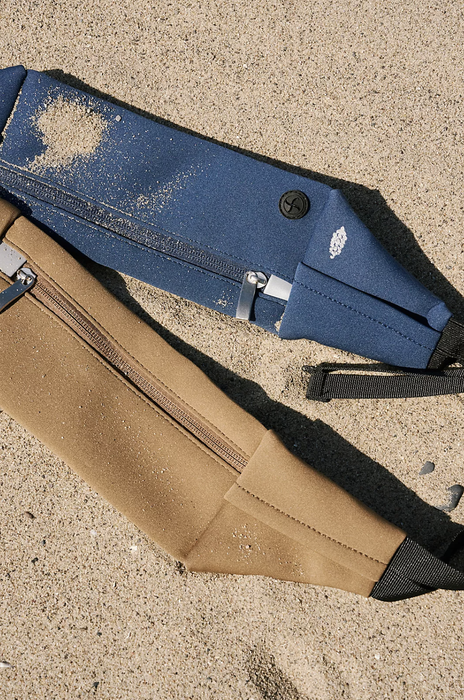 Two slings in tan and blue are resting on the sand.
