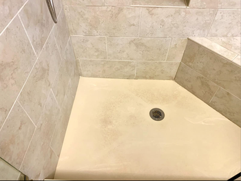 A shower with a yellow-stained floor in need of cleaning