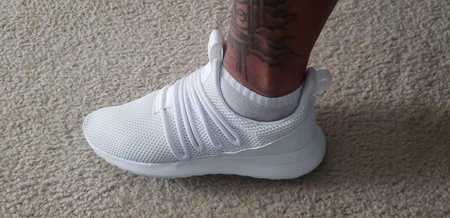 A reviewer sporting white laced shoes made from mesh fabric, complete with a loop on the heel