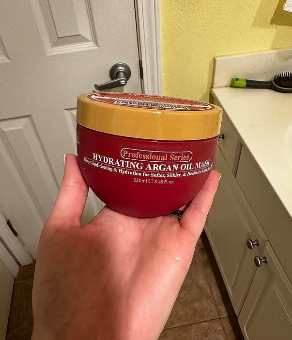 Image of a reviewer's hand holding a container of the hair mask