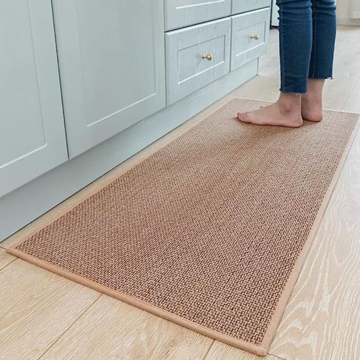 A person standing on a textured, neutral-toned rug in a kitchen with wooden flooring