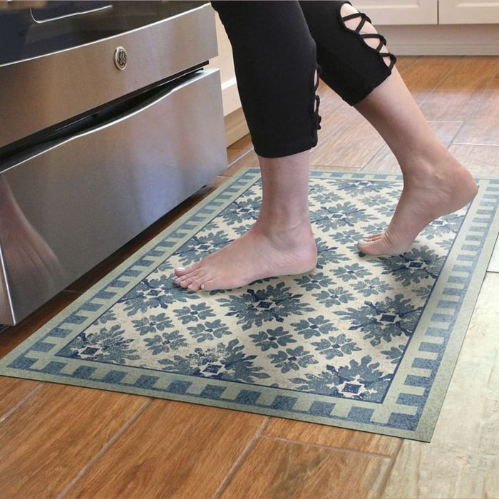 A person standing on a blue patterned floor mat placed on a wooden floor