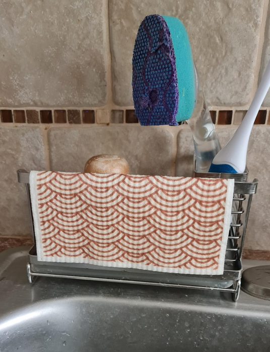 A wet Swedish dishcloth hanging over the edge of a sponge caddy next to the sink.