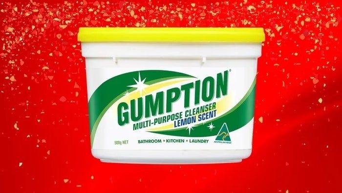 A tub of Gumption multi-purpose cleaner with a refreshing lemon scent set against a vibrant red, splattered background