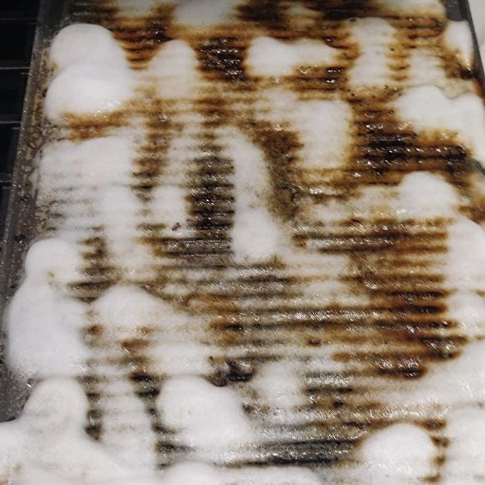 A dirty baking sheet covered in white cleaning foam