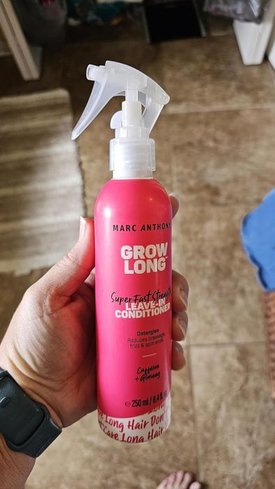 A hand holding a bottle of Marc Anthony Grow Long Super Fast Strength Leave-In Conditioner