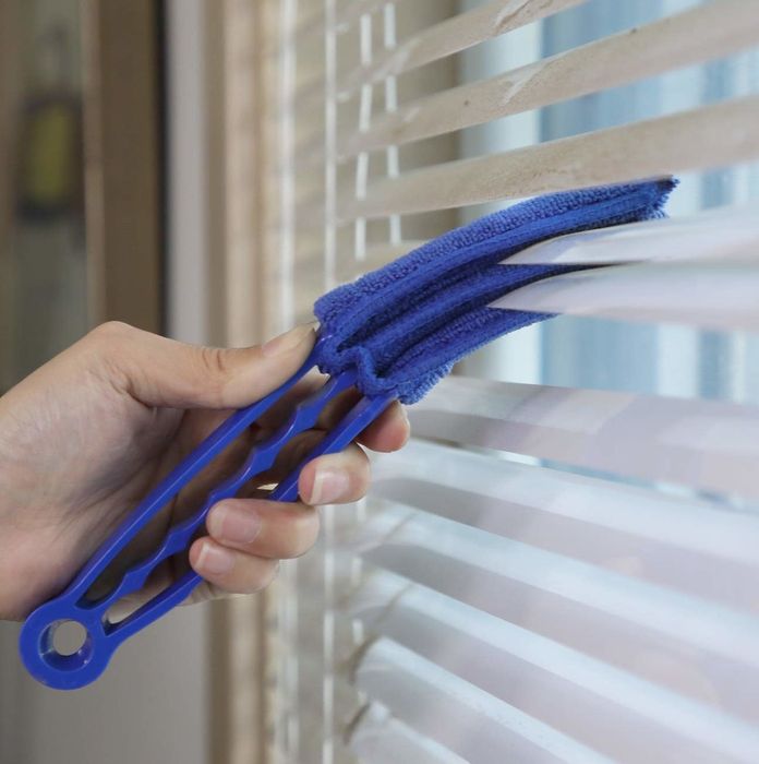 A hand using the duster on window blinds