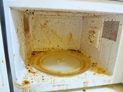 before image of a dirty microwave with food splatters and stains covering the interior walls and the rotating glass plate in the center