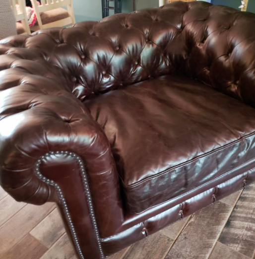 A reviewer admiring the transformation of a rejuvenated brown leather armchair, now looking fresh and bright.
