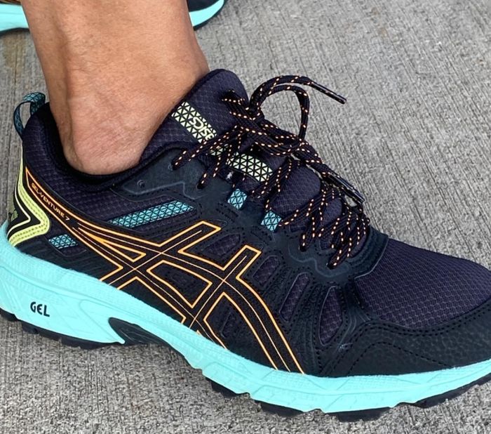 A reviewer sporting navy sneakers with an aqua-colored sole and a thicker gel heel.