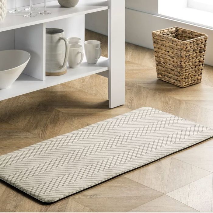 A neutral-toned chevron-patterned anti-fatigue mat placed on a wooden floor