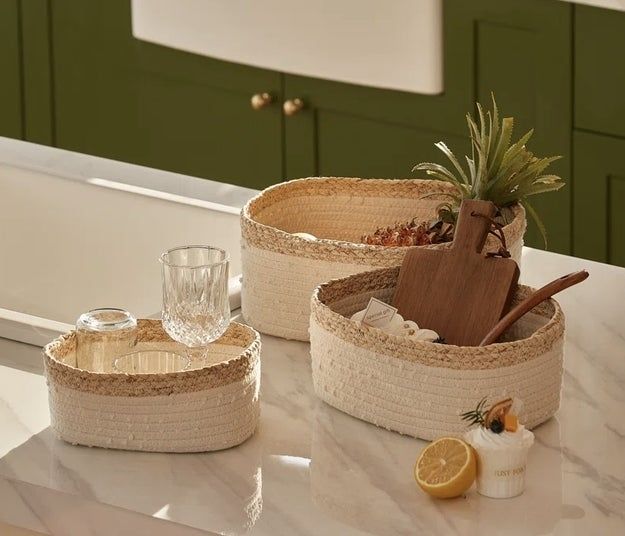 Three woven fabric baskets placed on a marble countertop, filled with assorted kitchen essentials