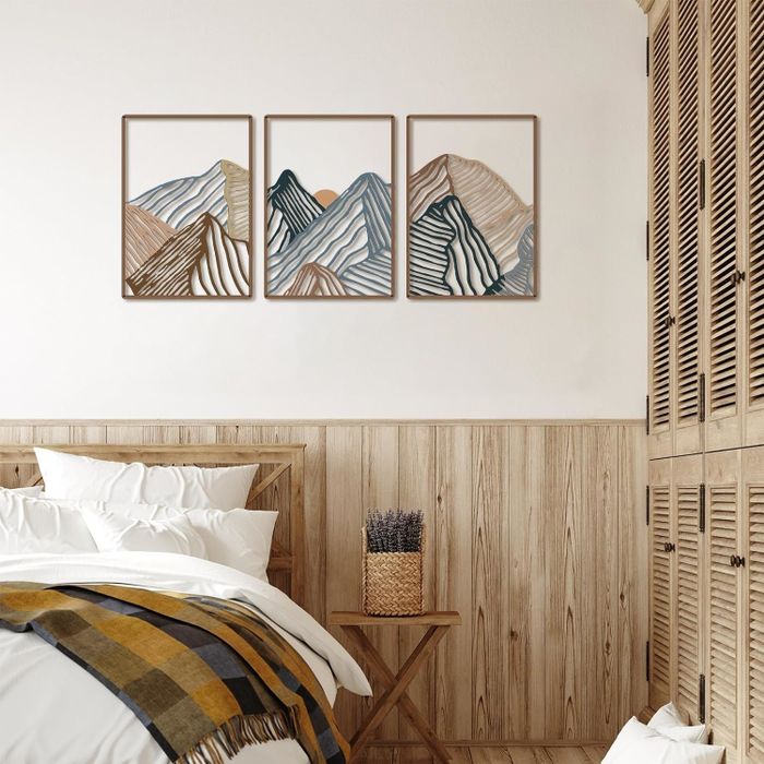 A trio of framed abstract mountain artworks displayed above a bed with a wooden headboard and a striped blanket