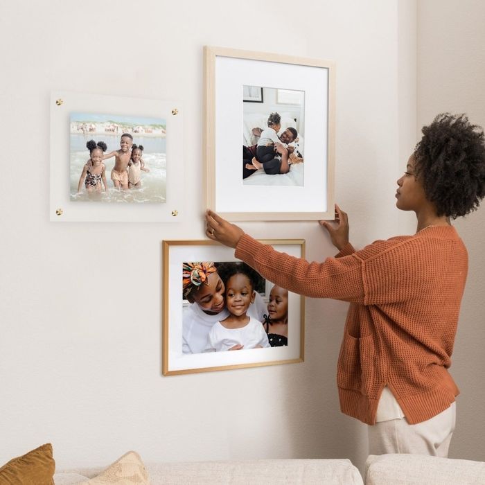 A person arranging three framed photos on a wall, capturing family memories for interior decoration