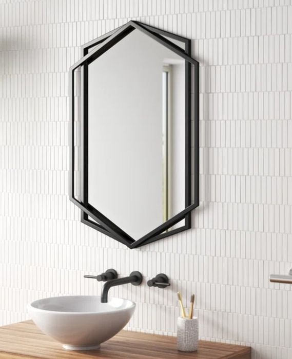 A bathroom featuring a geometric mirror, a sleek sink, and wall-mounted faucets