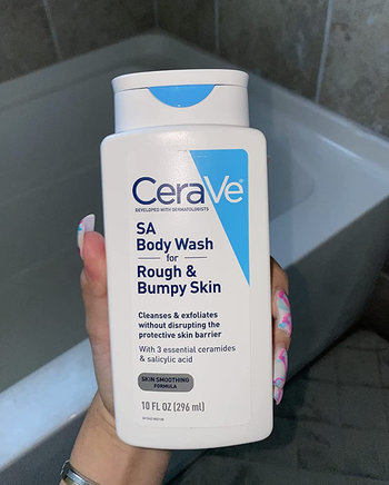 reviewer showcasing the body wash bottle beside the bathtub