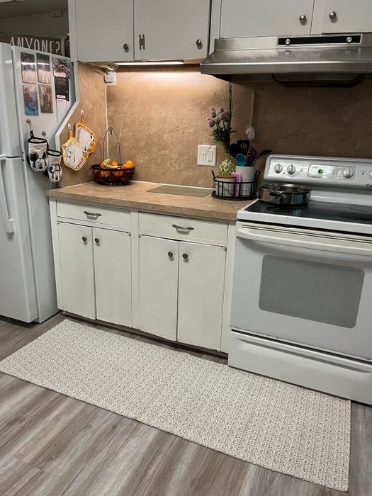 A modern kitchen featuring a white oven, stainless steel range hood, wooden cabinets, and a countertop adorned with a fruit basket and a wire basket holding utensils.