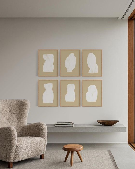Six framed silhouette artworks displayed on a wall above a sofa, accompanied by a side table and wooden stool in a minimalist room