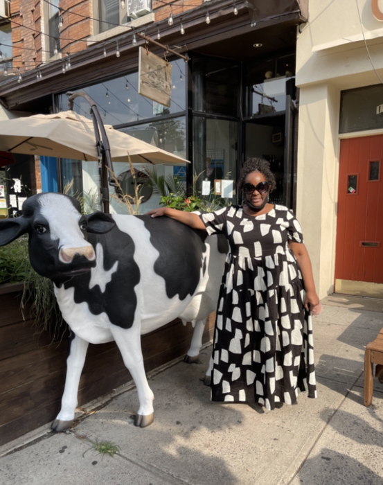 reviewer standing outside a cow-themed café, wearing a black and white dress